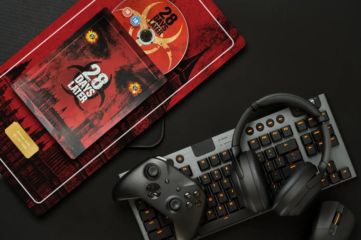 A styled flat-lay of a 28 Days Later themed gaming setup on a dark background, featuring a red and black mousepad with the movie title, a matching red and black DVD case, a black wireless gaming keyboard with orange backlighting, a black wireless controller, and over-ear headphones.