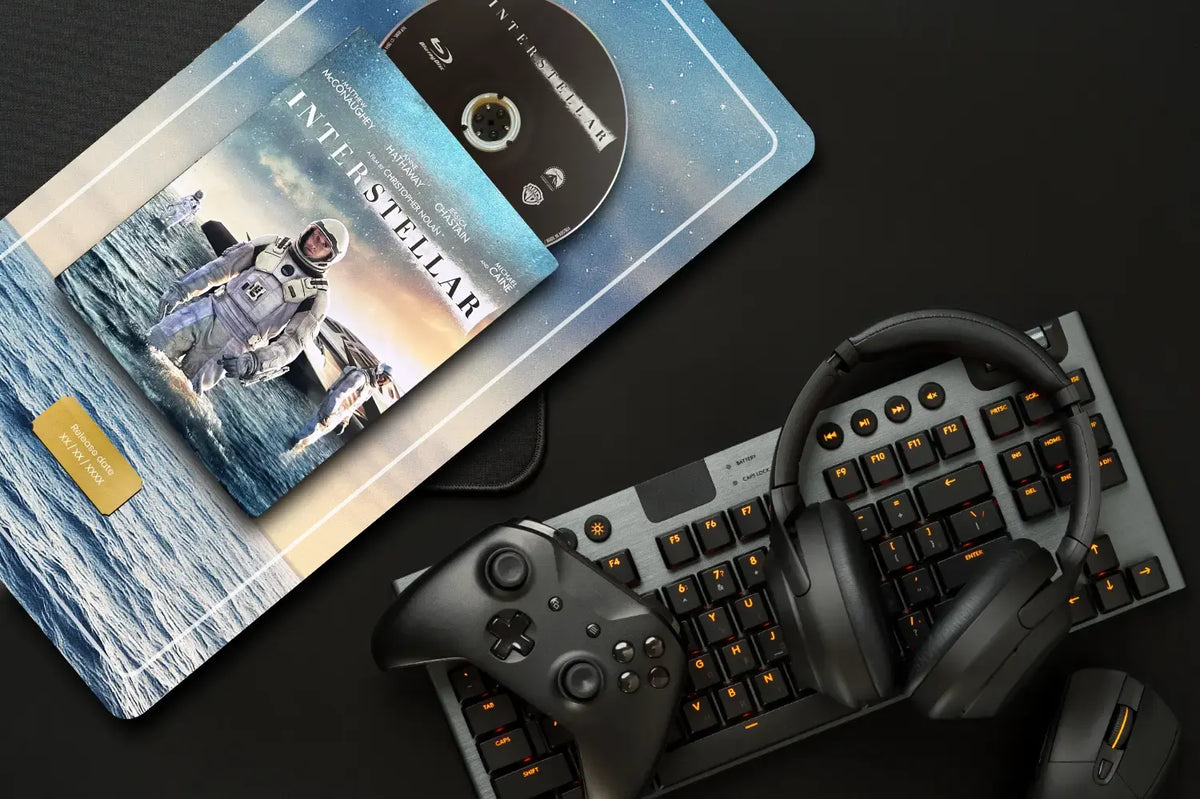 A styled flat-lay featuring a custom Interstellar-themed plate with an astronaut graphic and Blu-ray case, accompanied by a black mechanical keyboard, black over-ear headphones, a game controller, and a mouse on a dark background.