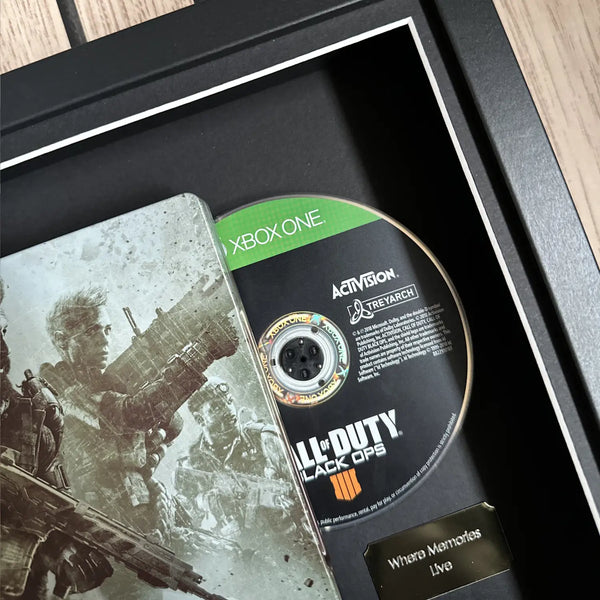 A framed and boxed presentation of the video game Steelbook edition of Call of Duty: Black Ops 4, featuring the game case, a single-player disc for Xbox One, and a small plaque inside a black shadowbox frame.