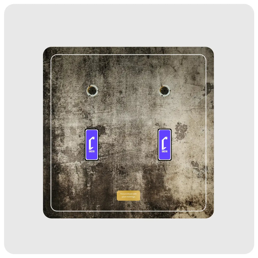 A square decorative wall plate featuring a distressed concrete texture in gray, brown, and black, with two small purple rectangular labels and a small gold label near the bottom. The item is centered on a light gray background.