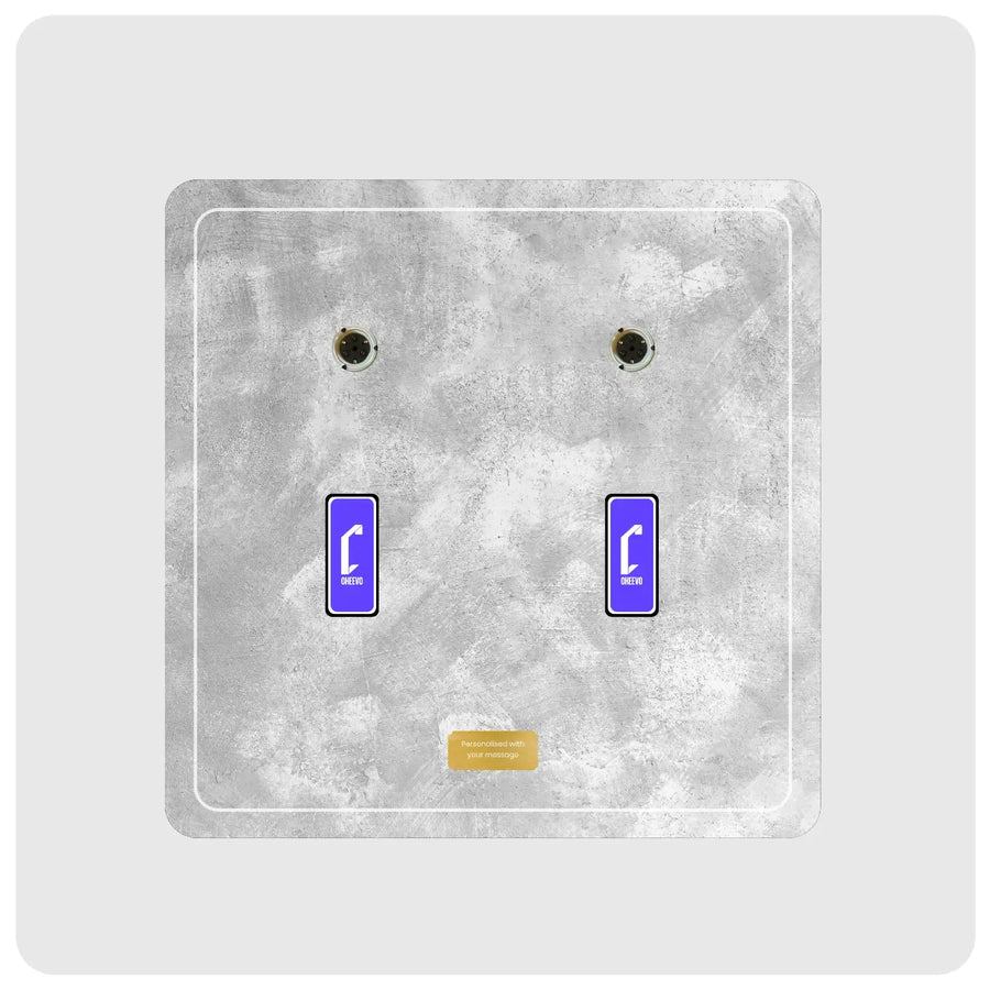 a modern artwork display plate featuring a textured gray concrete-style faceplate with two blue rectangular switches displaying white Cheevo logo and gold plate