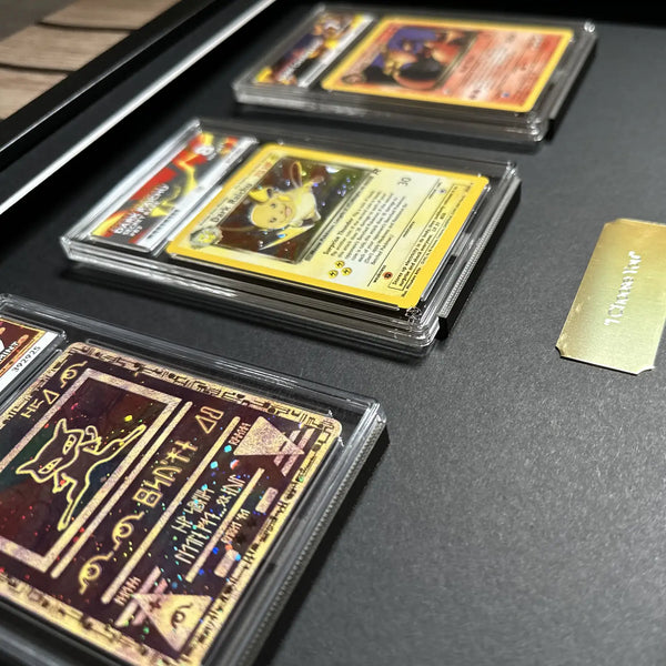 Several collectible trading cards in clear plastic protective cases arranged on a dark display surface, with a small gold card or tag visible to the right.